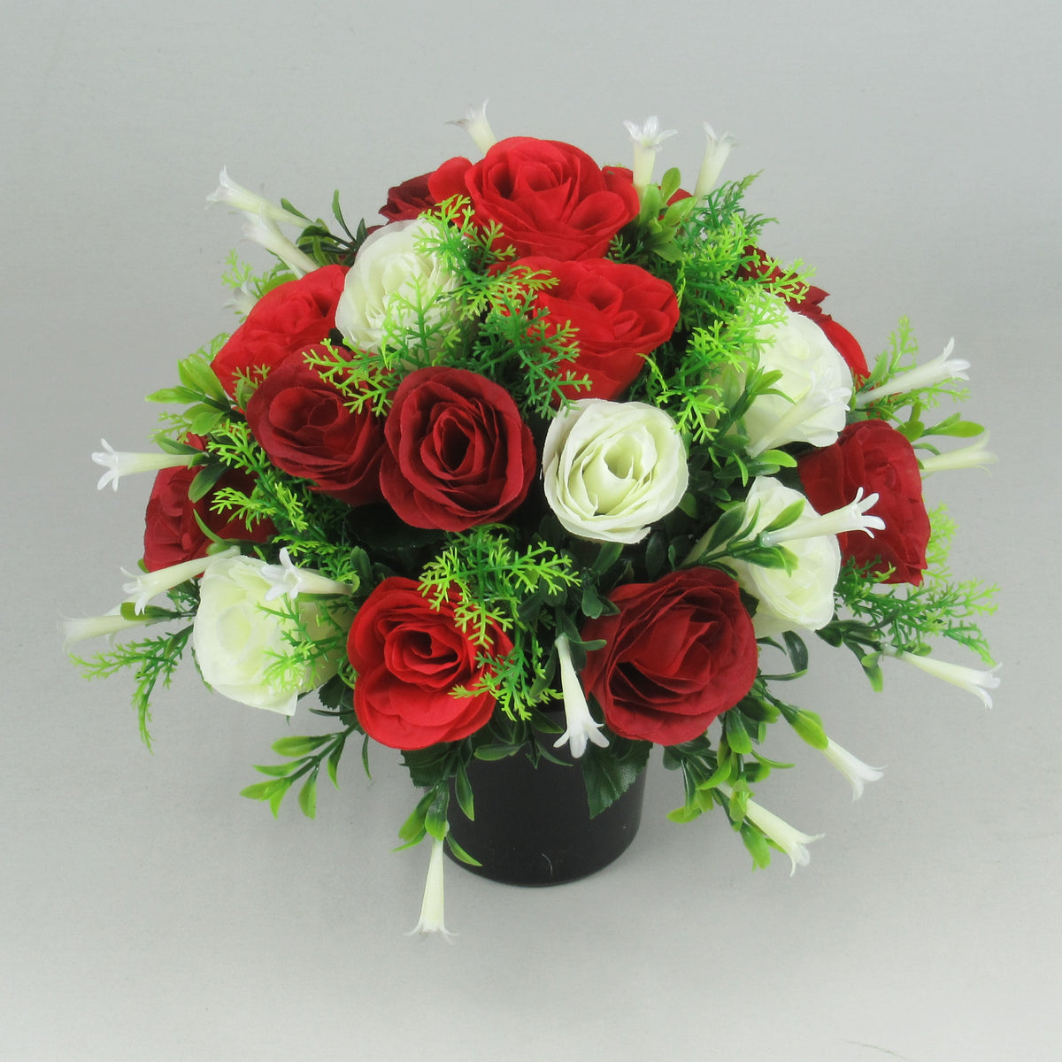 Artificial red and ivory rose arrangement with green foliage in a black pot