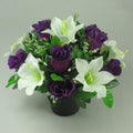 Artificial flower arrangement in black memorial pot with purple roses, white lilies, green foliage