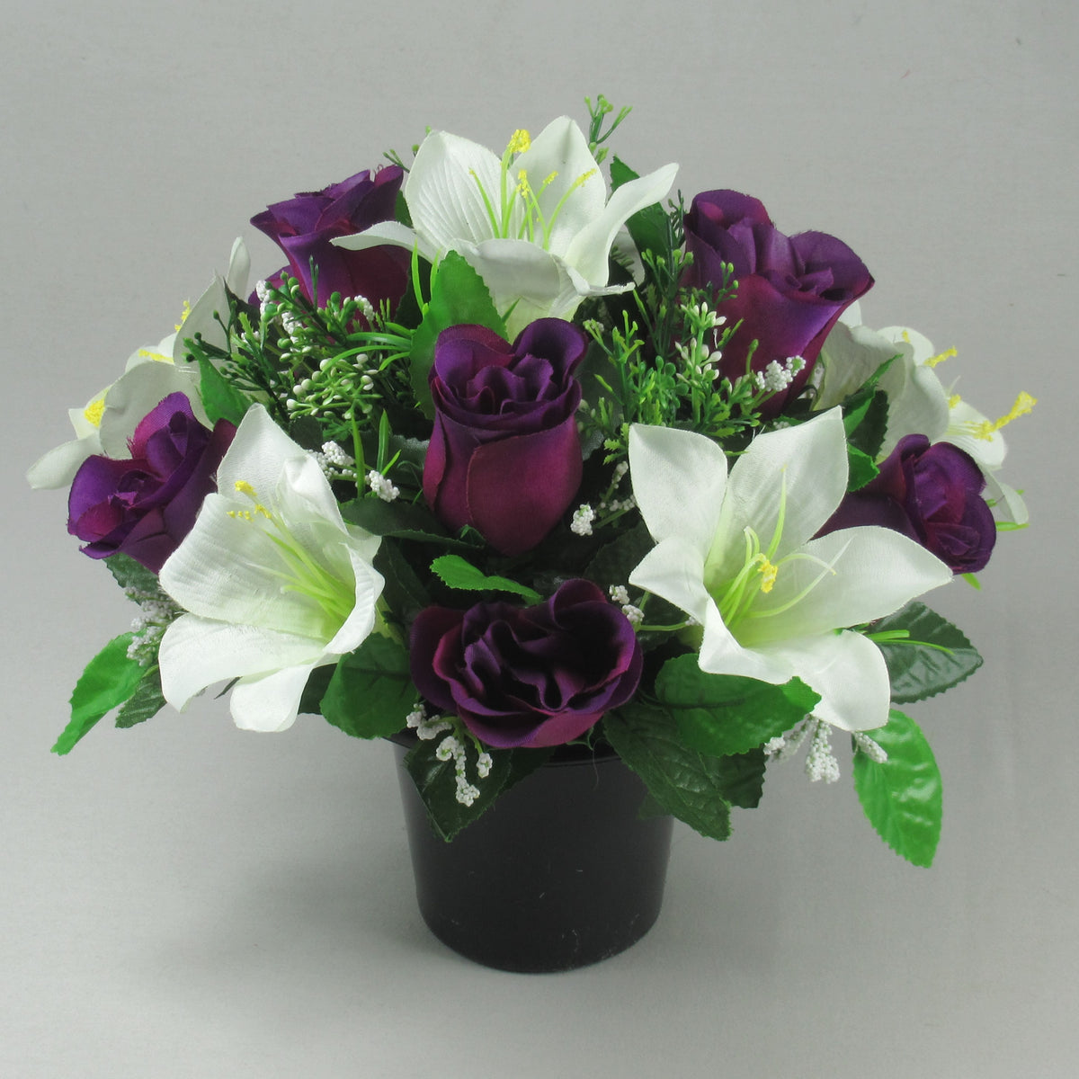 Artificial flower arrangement in black pot with purple rosebuds, white lilies, green leaves