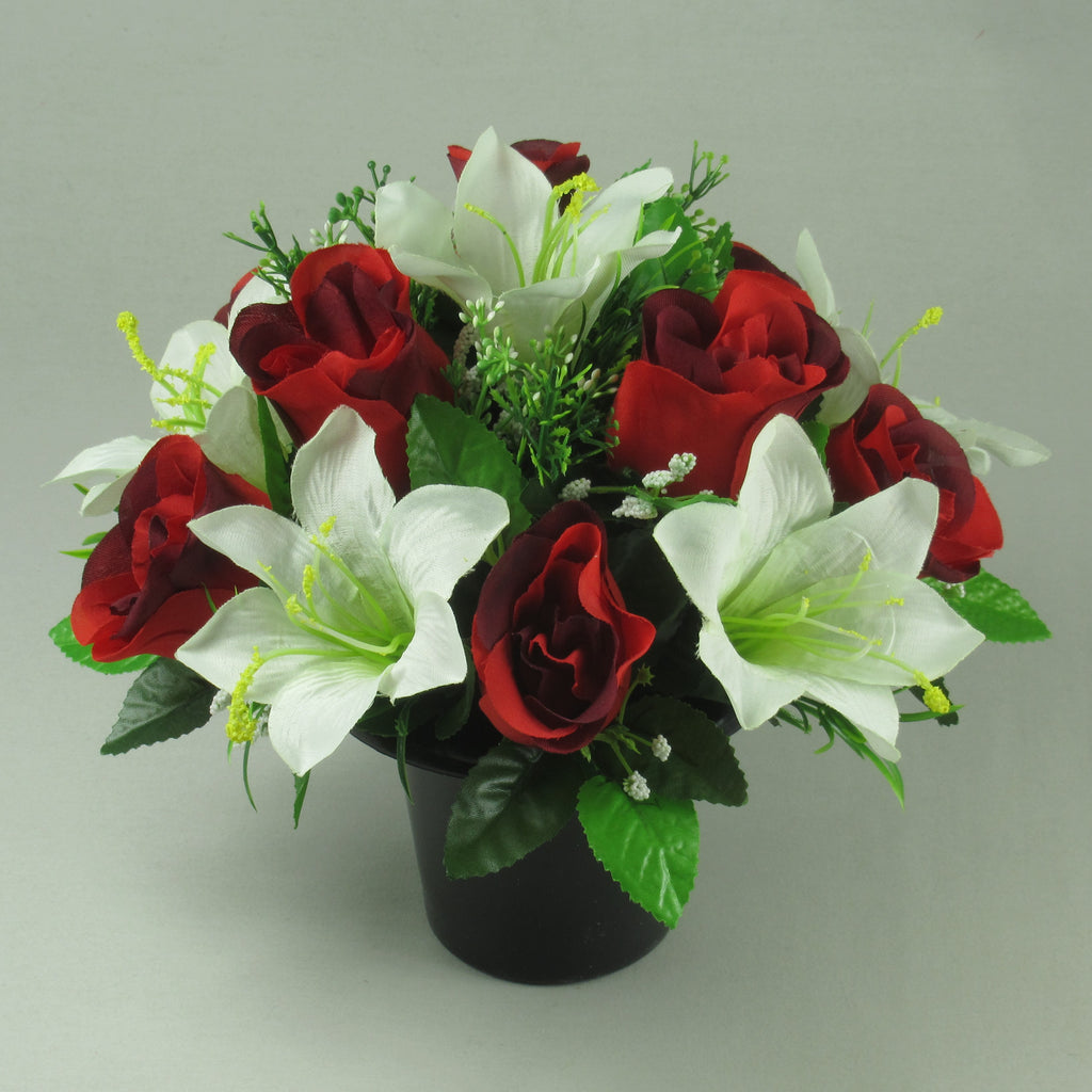 Artificial flower arrangement with red roses and ivory lilies with green foliage in black pot
