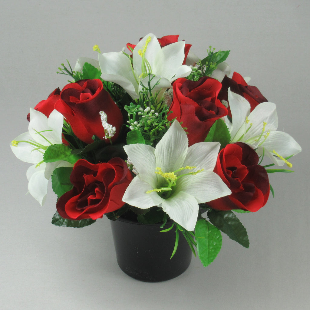 Artificial flower arrangement with red roses, ivory lilies, and greenery in black pot